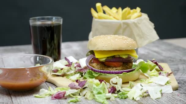 4 k κουκλίτσα βολή του burger, πατάτες τηγανητές, αναψυκτικά τύπου κόλα και κέτσαπ στο ξύλινο τραπέζι πάνω από το μαύρο φόντο - Πλάνα, βίντεο