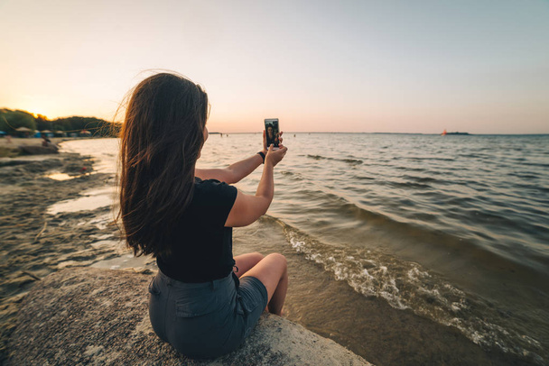 mujer se sienta en una playa y toma una foto de la playa
 - Foto, Imagen