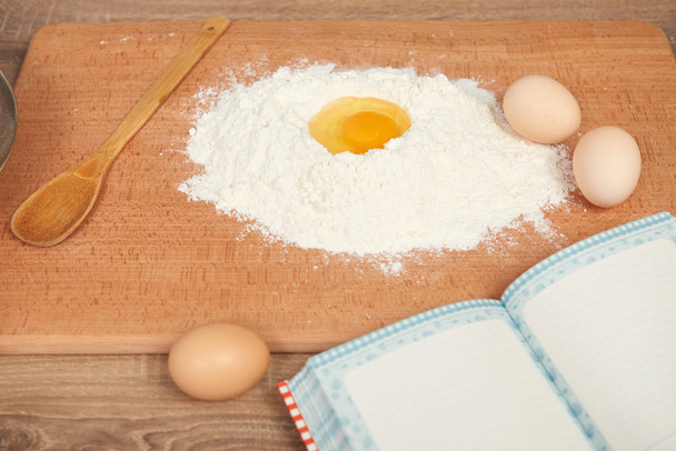 Flour heap and broken egg closeup for baking on a wooden background. Raw food and kitchen utensils. - Photo, Image