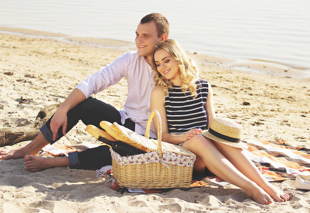 Eles estão apaixonados. Horizontal tiro de jovem e belo casal olhando para longe e sorrindo enquanto sentado na praia e fazendo piquenique
. - Foto, Imagem