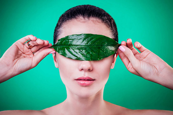 Uma mulher a cobrir os olhos com uma folha. Conceito de cosméticos orgânicos
 - Foto, Imagem
