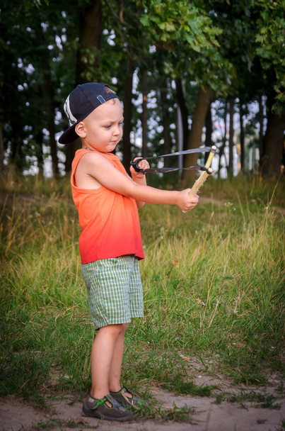 Boy in a cap plays a bully with a slingshot  - Photo, Image