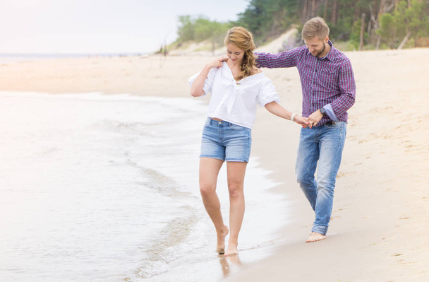恋ビーチ開催海に沿って歩く若いカップル  - 写真・画像