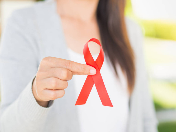 Closeup woman hand holding red ribbon HIV, world AIDS day awareness ribbon.  Healthcare and medicine concept. - Photo, Image