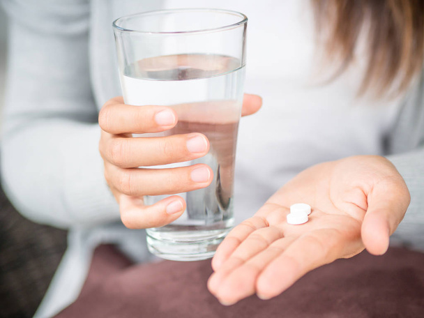 Mão de mulher close-up com comprimidos comprimidos de medicamentos e vidro de água para tratamento de dor de cabeça. Saúde, conceito de suplementos médicos
 - Foto, Imagem