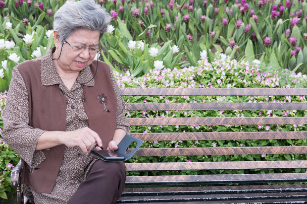 Aasian vanhempi nainen tilalla mobiili älypuhelin istuessaan olla
 - Valokuva, kuva