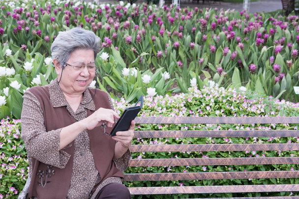 Aziatische oudere vrouw met mobiele smartphone zittend op worden - Foto, afbeelding