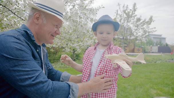 Chlapec a děda hraje dřevěné letadlo na trávníku - Záběry, video