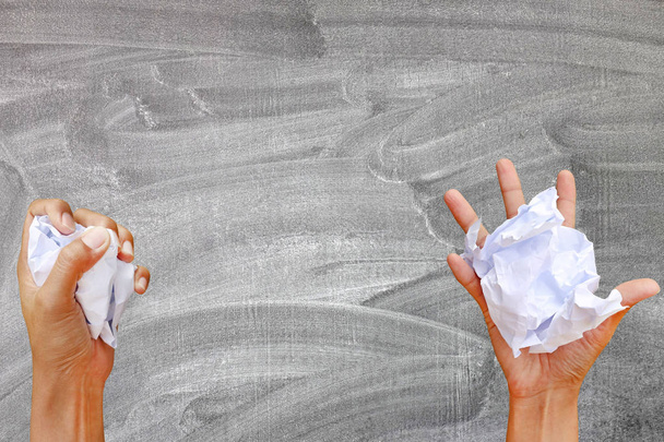 Hand holding crumpled paper against blackboard background. - Foto, imagen