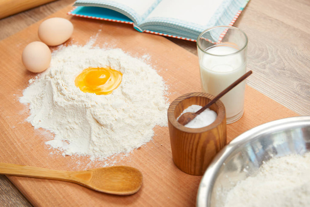 Mehl und zerbrochene Eier zum Backen auf einem hölzernen Hintergrund. Rohkost und Küchenutensilien. - Foto, Bild