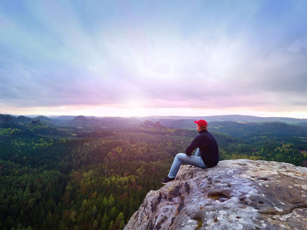 Шукаю горизонт. Чоловік сидить на скелі над густими лісами або джунглями і насолоджується видом
. - Фото, зображення