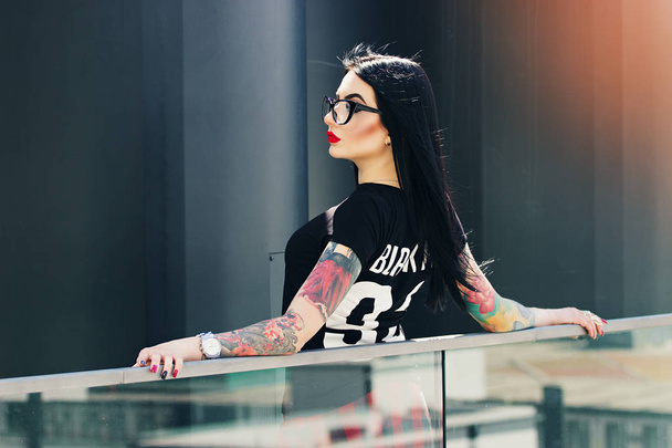 Tattoed fashion. Portrait of attractive tattooed hipster girl posing to camera against urban background. - Photo, image
