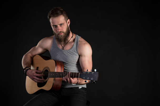 Karismaattinen mies, jolla on parta ja joka soittaa akustista kitaraa mustalla taustalla. Vaakakehys
 - Valokuva, kuva