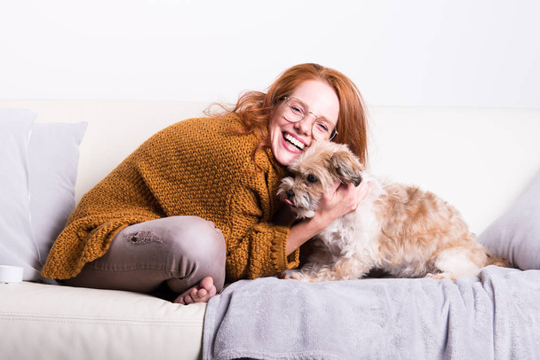 Beautiful, red-haired woman with her dog on the couch - Photo, image