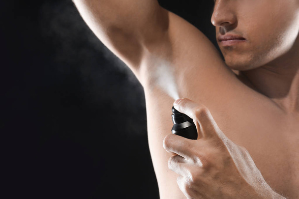 Handsome young man with deodorant on dark background - 写真・画像