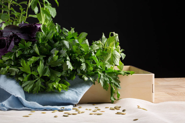 Fresh and aromatic herbs in a paper box on a black background. Organic branches of parsley and basil on a table. - Foto, imagen