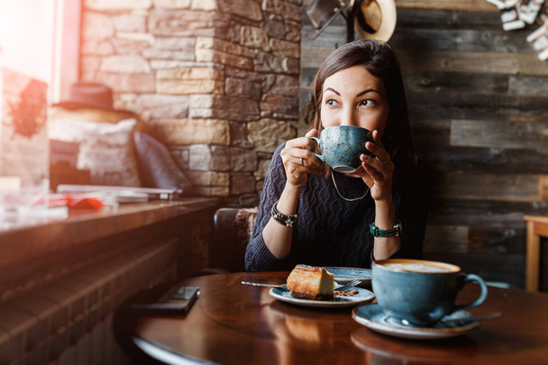 Una hermosa mujer asiática bebiendo café caliente o té de la taza vintage en la moderna cafetería loft
 - Foto, Imagen