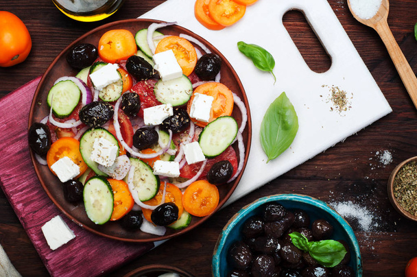 Mediterranean cuisine. Salad from tomatoes, cucumbers, purple onions and dried olives on a brown plate on a dark background. Fusion Greek salad. Tasty and healthy seasonal dish. - Foto, Imagen