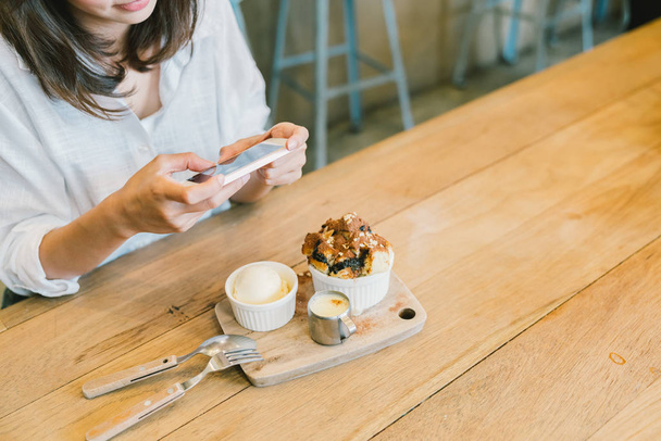 Asian girl taking photo of chocolate toast cake, ice-cream, and milk at coffee shop. Dessert or food photograph hobby. Smartphone or mobile phone photography habit concept. With copy space - Foto, Imagen