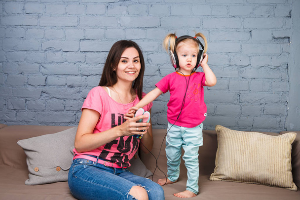 Mãe e filha ouvir música em fones de ouvido grandes colocar em sua cabeça, sentado no sofá. Segura o telefone
. - Foto, Imagem