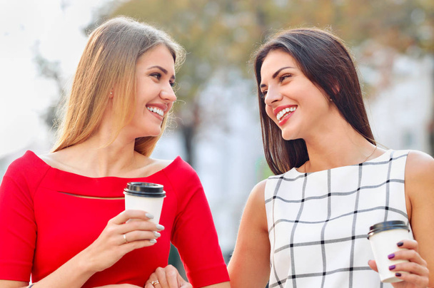 Attractive young women drink take away coffee in summer city - Foto, imagen