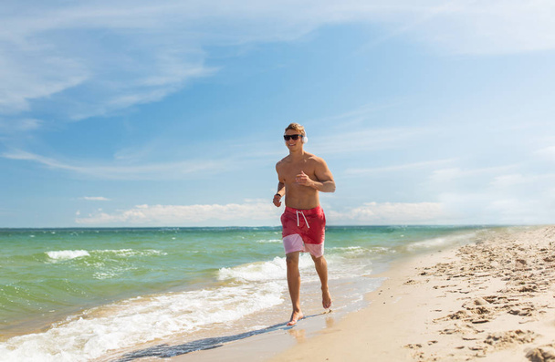 happy man with headphones running along beach - Foto, Imagem