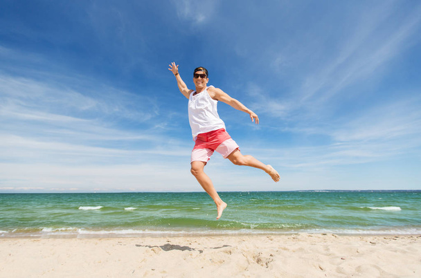 smiling young man jumping on summer beach - Fotoğraf, Görsel
