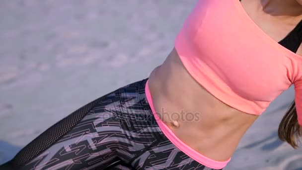 Healthy, young beautiful woman doing exercises for oblique abdominal press muscles,, on the beach, at sunrise, Makes exercises for balance and coordination, deep muscle tone. - Footage, Video