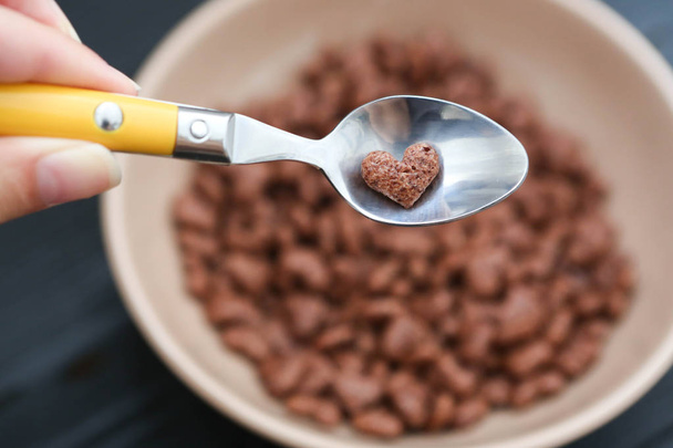 Cornflake heart shaped is lying on the spoon on the cornflakes background - Photo, image