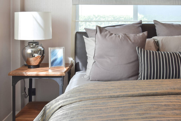 stilvolles Schlafzimmer-Interieur mit gestreiften Kissen auf dem Bett und dekorativer Tischlampe. - Foto, Bild