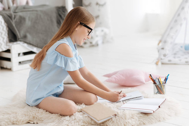 Excited girl doing homework on faux fur carpet - Photo, Image