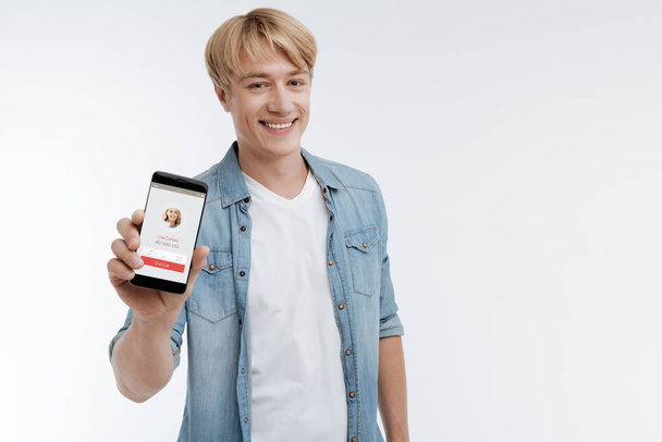Smiling young man demonstrating his telephone - Foto, Bild