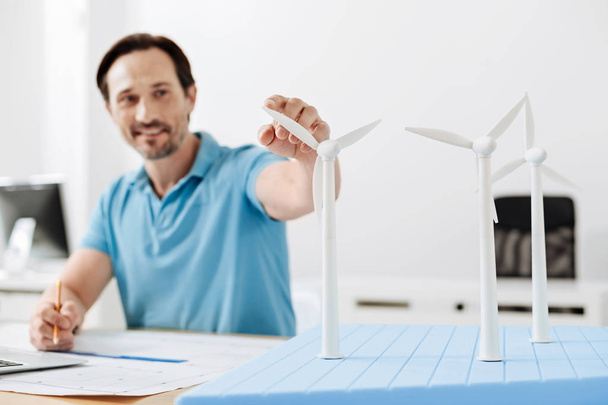 Bristled man touching a wind turbine sail while drawing blueprint - Zdjęcie, obraz