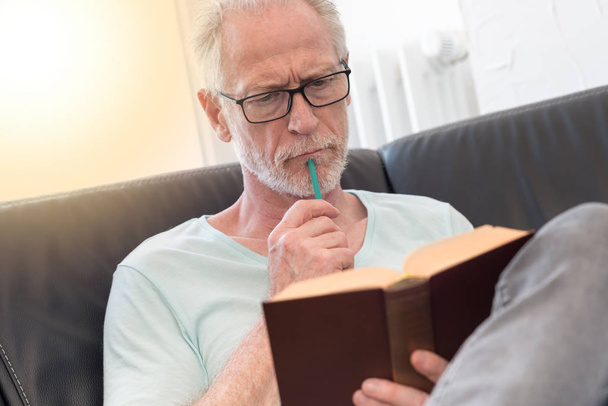Portrait of thoughtful mature man reading a book, light effect - Zdjęcie, obraz