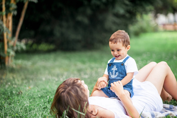 Äiti ja nuori poika leikkivät ruoholla. Onnellinen perhe kävelee puistossa. Äiti ja poika syövät hedelmiä. Piknikille. Kesä
. - Valokuva, kuva