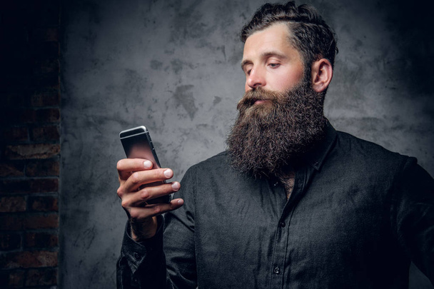 Бородатий чоловік тримає смартфон
 - Фото, зображення