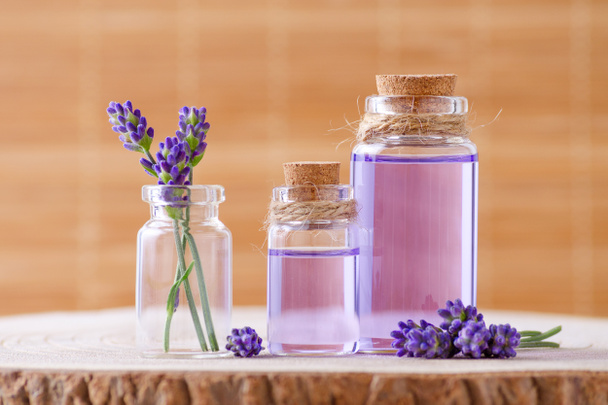 aceite esencial en botellas de vidrio y flores frescas de lavanda sobre un tocón y un fondo marrón
 - Foto, imagen