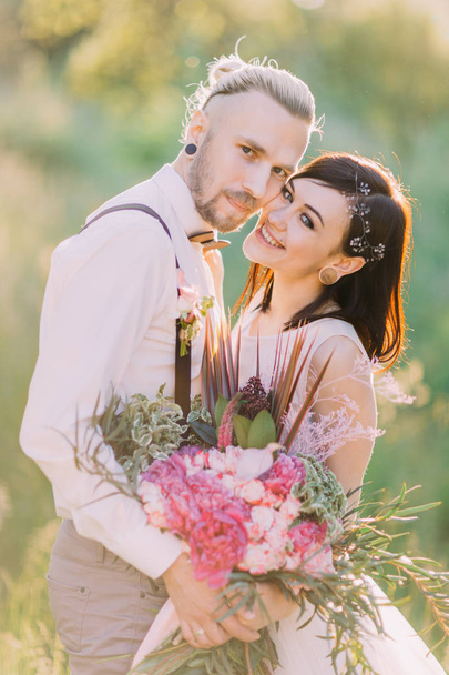 Smiling newleweds and holding the big bouquet of flowers in the sunny spring. - Photo, image