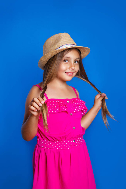 Portrait of young cute girl in pink dress and hat on blue background .Summer vacation and travel concept - Fotografie, Obrázek