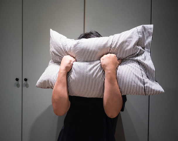 Depressed man covering his face with pillow and screaming in ang - Photo, Image