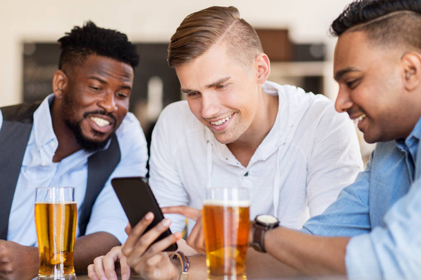 male friends with smartphone drinking beer at bar - Фото, зображення