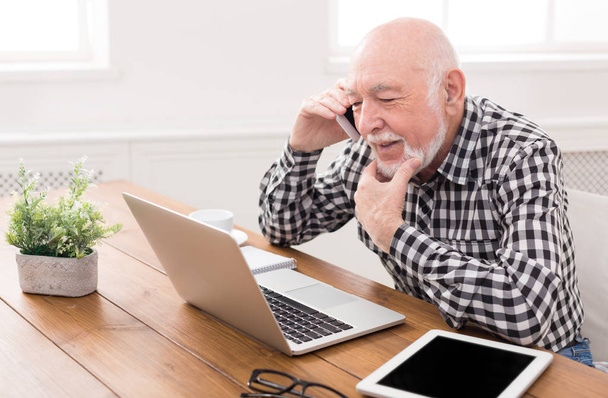 Vanhempi mies puhuu puhelimessa kannettavan tietokoneen kanssa
 - Valokuva, kuva