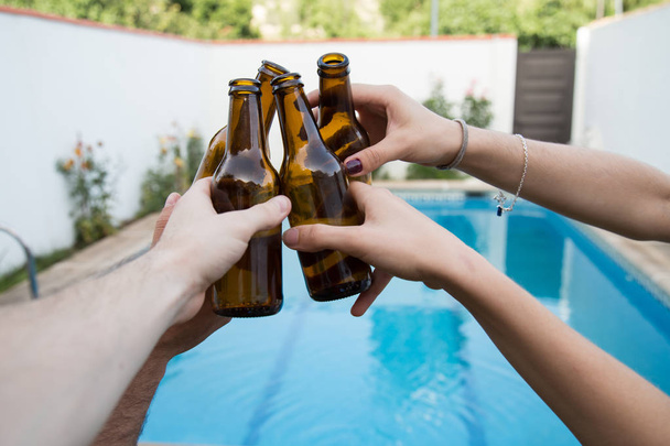 Hands of some friends toasting with beer bottles in the pool  - Photo, Image