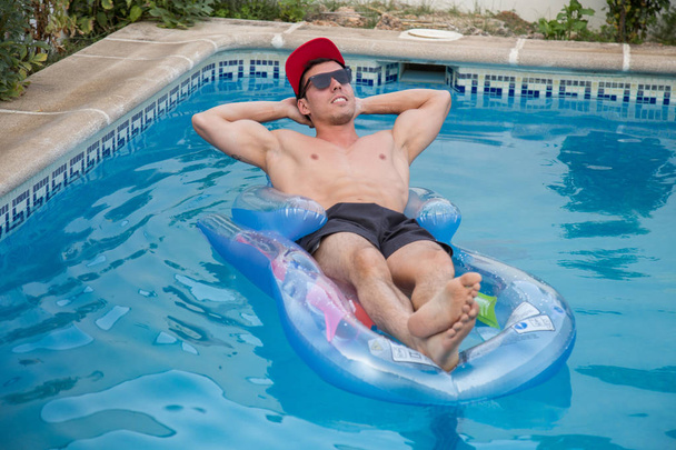 Starker junger Mann genießt das Leben und badet in einem aufblasbaren Floß im Pool - Foto, Bild