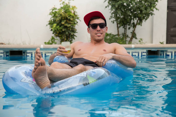 Joven hombre fuerte bebiendo cerveza en una cama de aire en la piscina
 - Foto, imagen