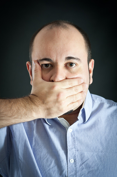 Man stopping up the mouth on dark background - Foto, Imagen