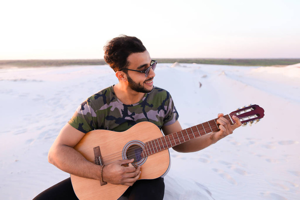 Lindo joven árabe macho disfruta del sonido de la guitarra, sentado en la colina en
 - Foto, imagen