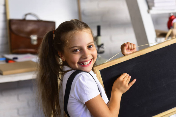 Girl with smiling face expression near desk with school supplies - Фото, зображення