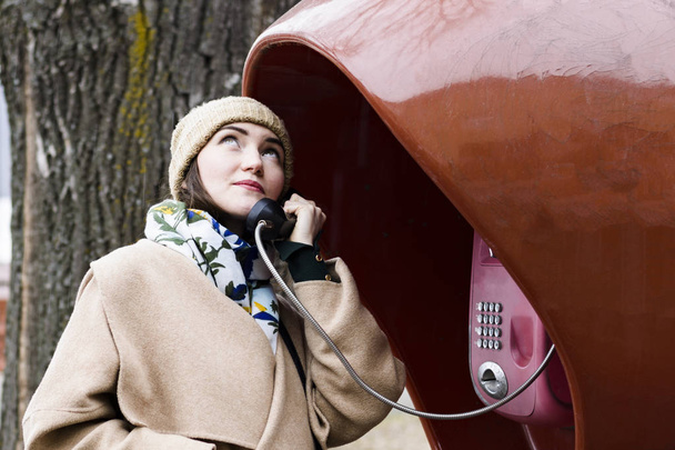 молода жінка посміхається і розмовляє на громадському телефоні
 - Фото, зображення