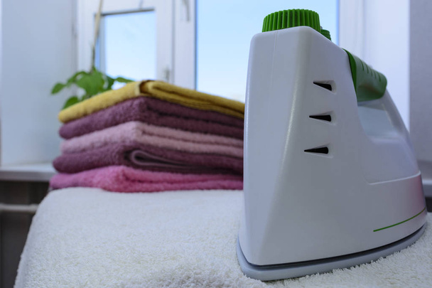 Ironing linen with steam generator. A stack of ironed towels lying next to the iron. Teflon sole plate covered with small holes - Fotoğraf, Görsel